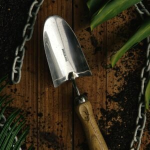 Top view of a garden trowel on wooden surface surrounded by soil and leaves.